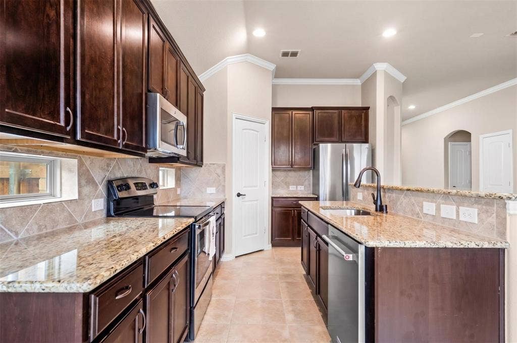 Modern kitchen featuring dark wood-finish cabinetry, light granite countertops, stainless steel appliances, a tiled backsplash, and recessed lighting