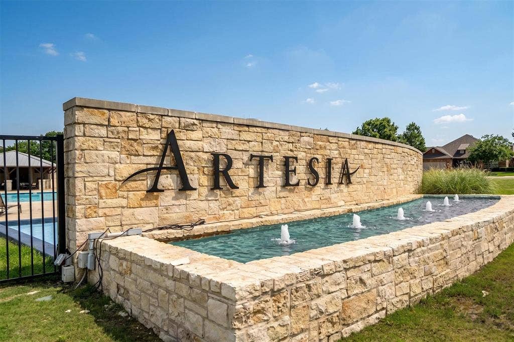 Stone-clad entry wall featuring "ARTESIA" lettering with an integrated water feature and multiple fountains