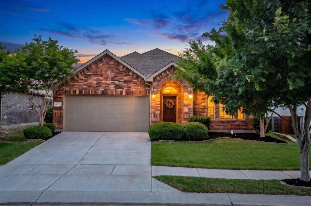 Brick facade residence featuring an arched entryway, attached garage, concrete driveway, and established landscaping with mature trees