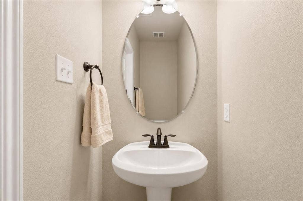 Pedestal sink with oil-rubbed bronze faucet and hardware, set below an oval mirror