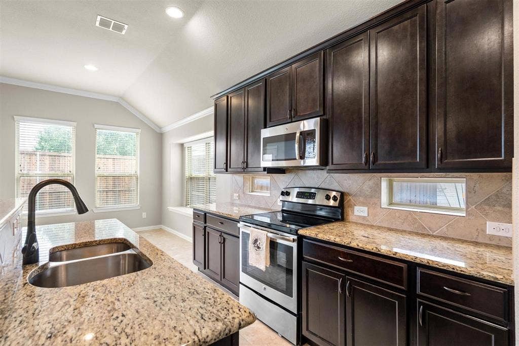 Kitchen featuring granite countertops, dark wood-finish cabinetry, stainless steel appliances, and a tile backsplash