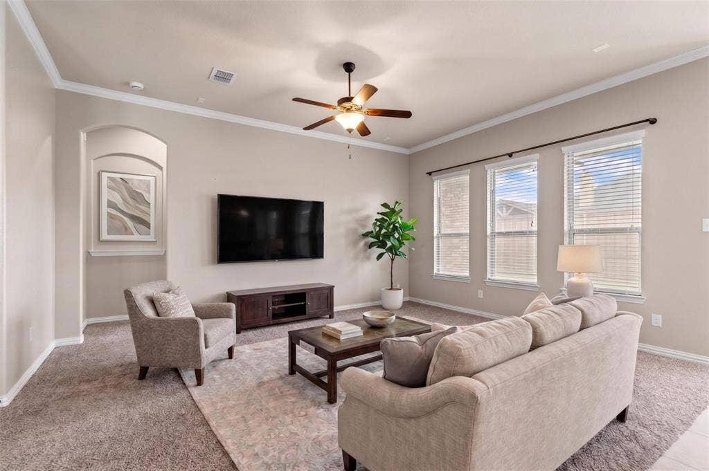 Spacious living area featuring neutral-toned walls, crown molding, and a ceiling fan with integrated lighting