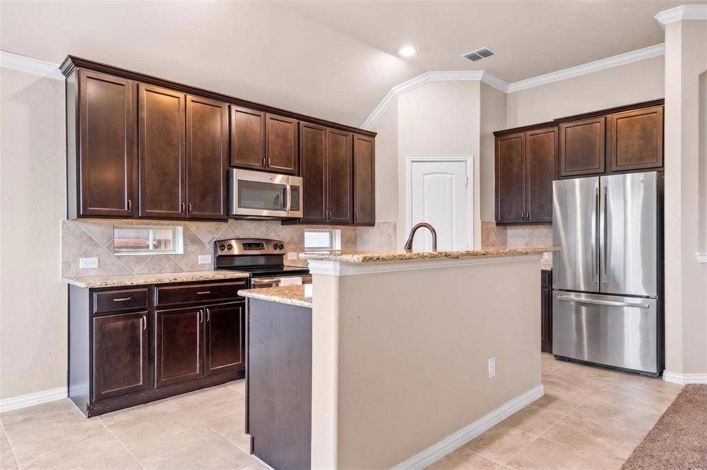 Kitchen featuring dark wood cabinetry, stainless steel appliances, light-colored granite countertops, and a tile backsplash