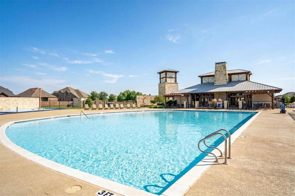 Expansive swimming pool with concrete decking, featuring a stone and wood beam amenity center with a prominent stone chimney and a detached stone tower