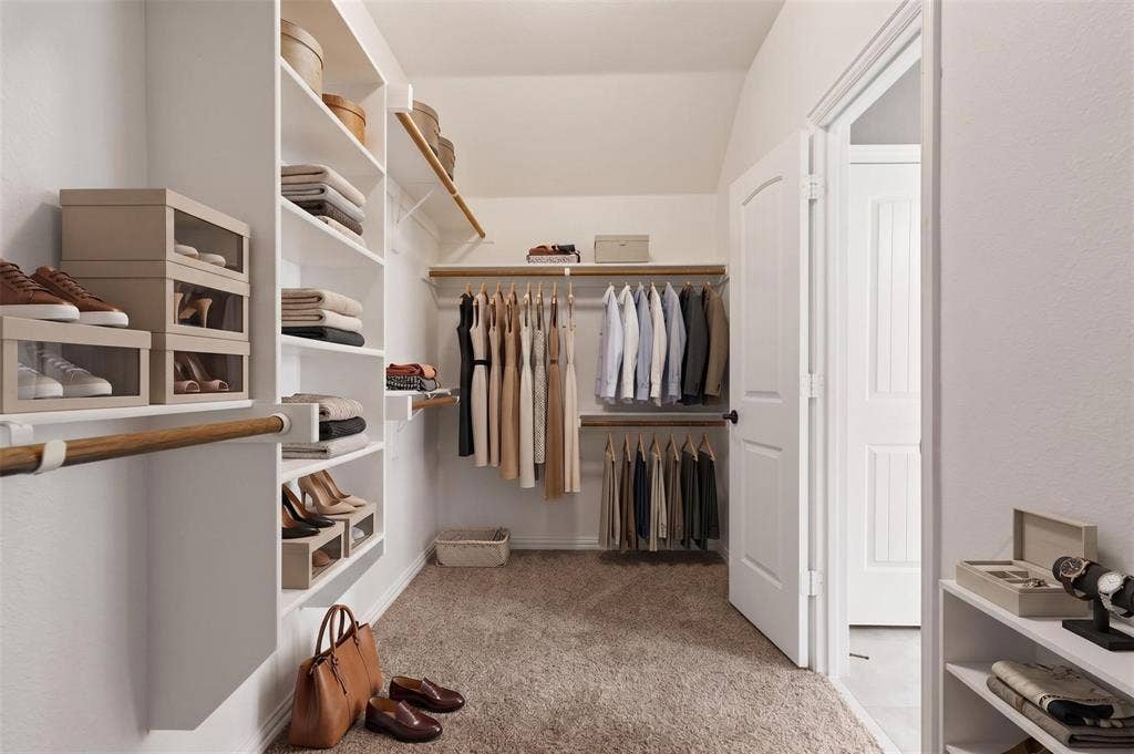 Spacious walk-in closet featuring extensive built-in shelving, multiple hanging rods, durable carpet flooring, and a paneled interior door