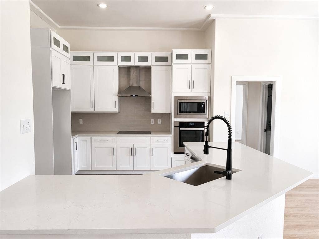 1706 Fairhaven Drive, Mansfield, TX 76063 Kitchen featuring white shaker cabinetry, stainless steel appliances, a tile backsplash, light-toned countertops, and a kitchen island with a black faucet