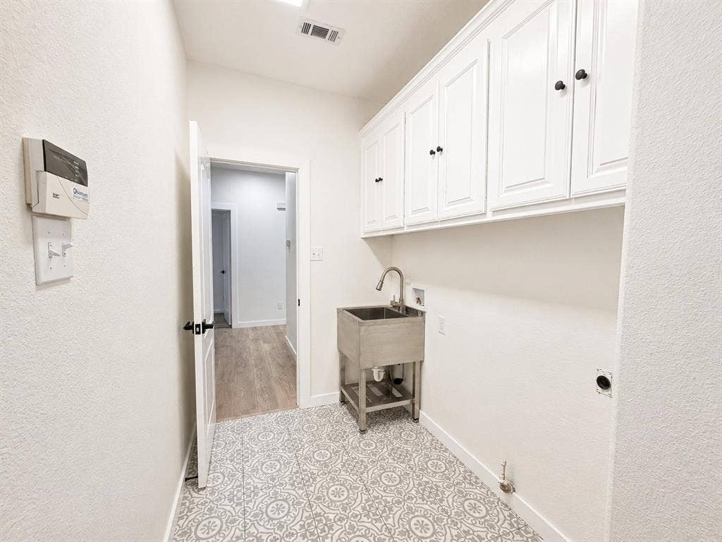 1706 Fairhaven Drive, Mansfield, TX 76063 Laundry area featuring patterned floor tiles, white shaker-style cabinetry, a stainless steel utility sink with a gooseneck faucet, and light neutral wall paint