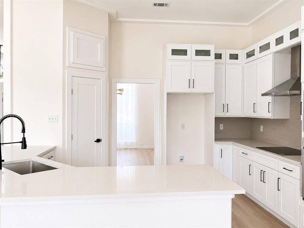 1706 Fairhaven Drive, Mansfield, TX 76063 Modern kitchen featuring white shaker cabinetry, light-toned countertops, stainless steel range hood, and a deep undermount sink with a matte black pull-down faucet