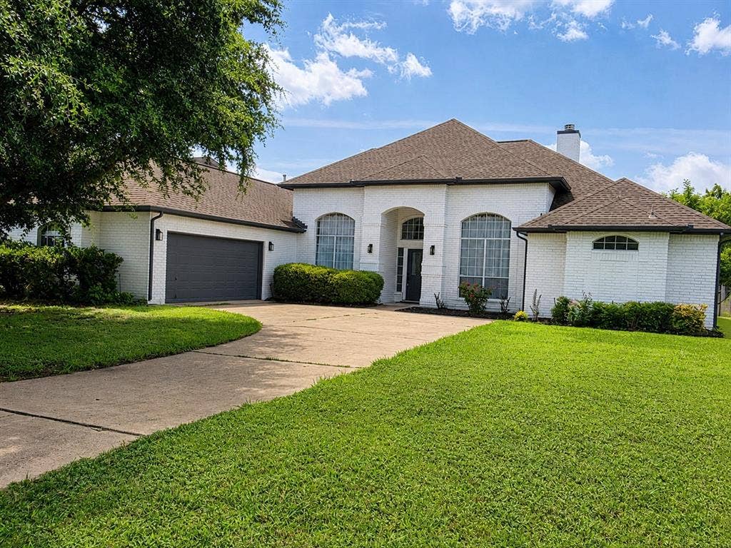 1706 Fairhaven Drive, Mansfield, TX 76063 White brick exterior with a dark brown shingle roof, featuring a two-car garage with a dark gray door, arched windows, and a paved driveway