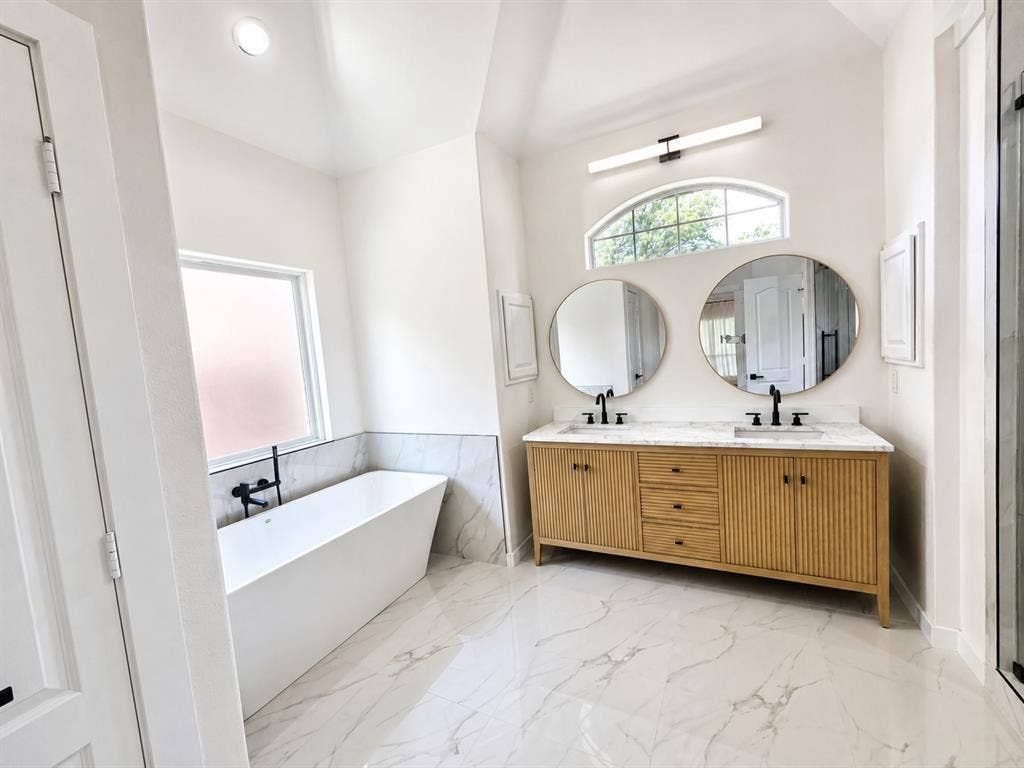 1706 Fairhaven Drive, Mansfield, TX 76063 Spacious bathroom featuring a freestanding tub with wall-mounted fixtures, a dual vanity with a light wood-finish base and stone countertop, and large-format porcelain tile flooring