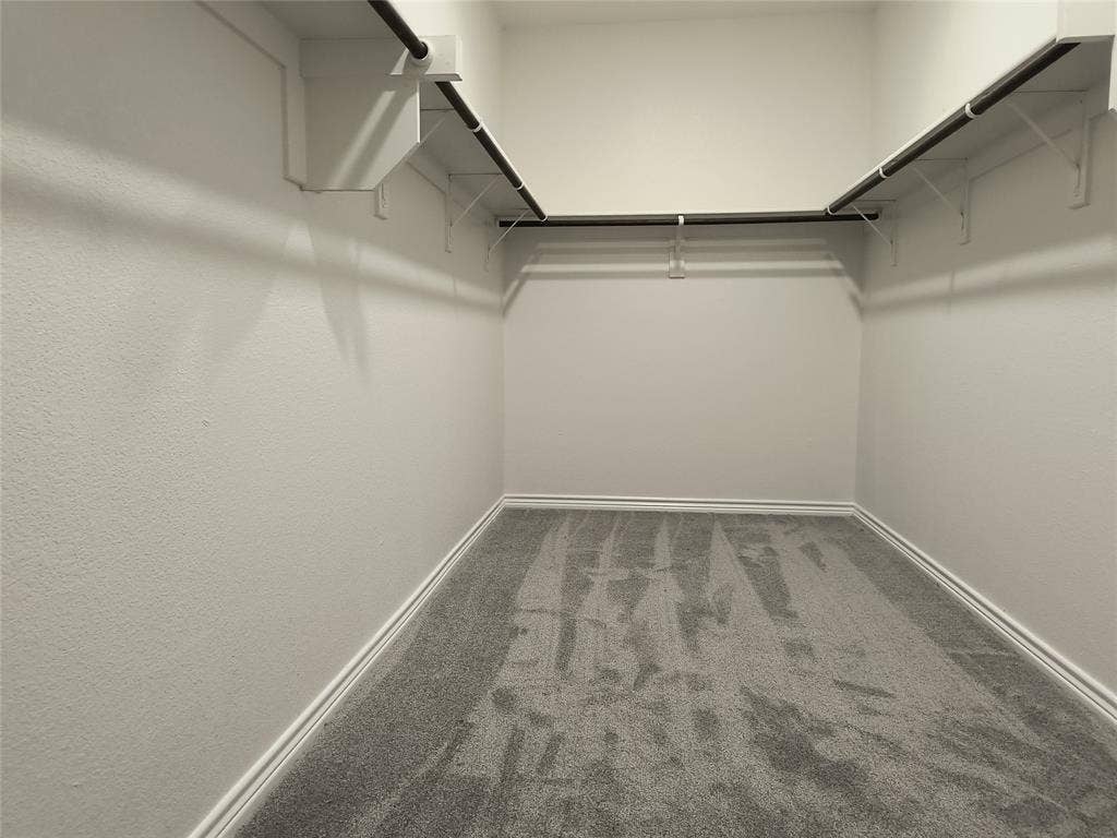 Walk-in closet featuring light gray carpeting, white baseboards, and white textured walls