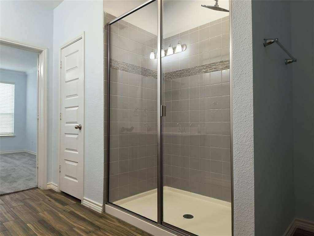 Spacious shower enclosure with glass doors, contemporary gray tile surround, decorative accent tile band, and overhead shower fixture