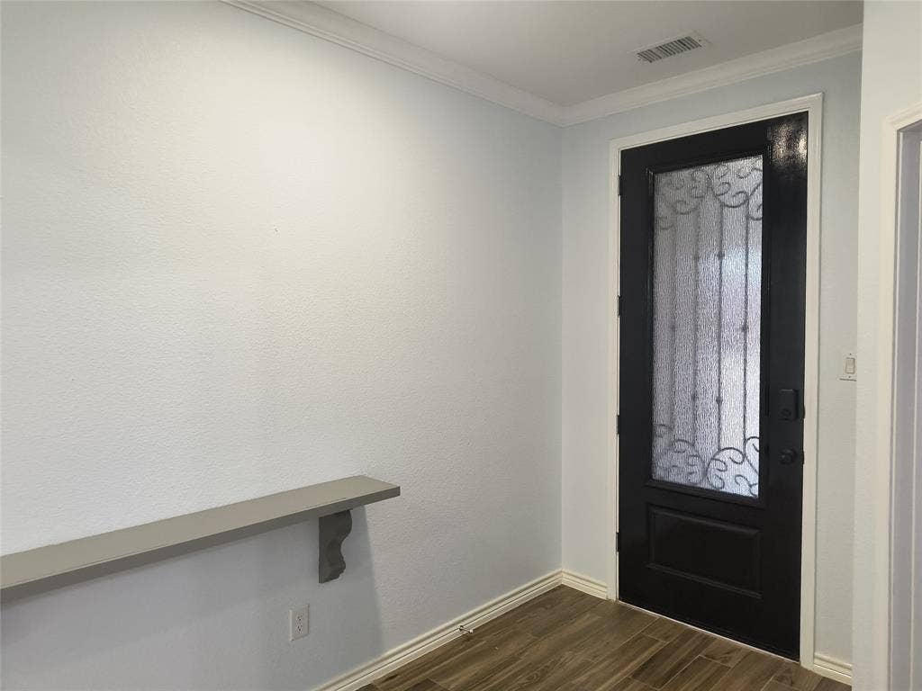 Black entry door with frosted glass and decorative ironwork, complemented by light wood-finish flooring