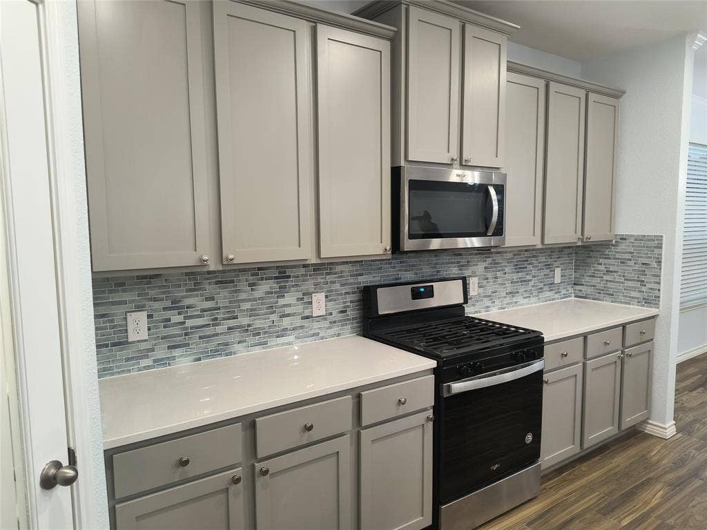Kitchen featuring wood-finish flooring, a central island, grey cabinetry, a mosaic tile backsplash, and stainless steel appliances including a microwave and range