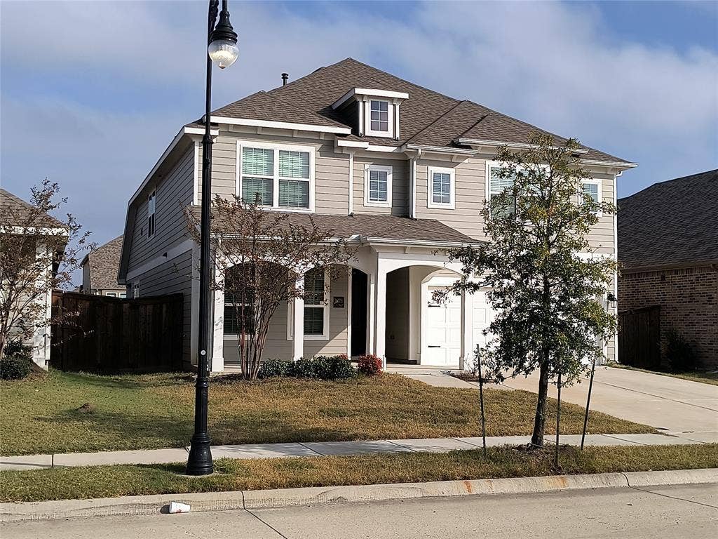 Two-story residence featuring light gray siding with white trim, a brown shingle roof, and an integrated two-car garage