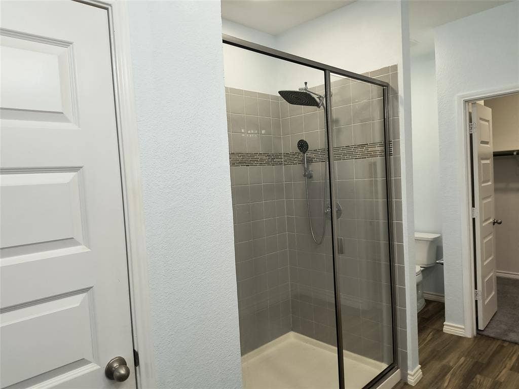 Glass-enclosed shower featuring a rainfall showerhead, handheld sprayer, and tiled walls with a decorative mosaic accent band