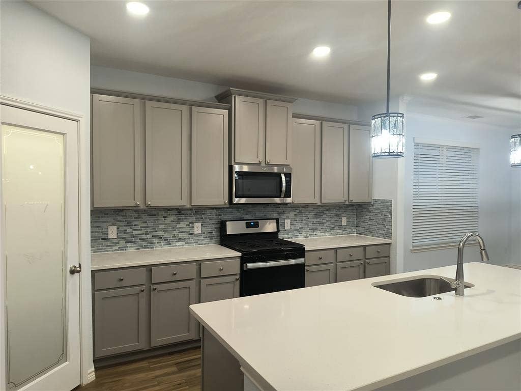 Contemporary kitchen featuring light gray cabinetry, a mosaic tile backsplash, and light-toned countertops