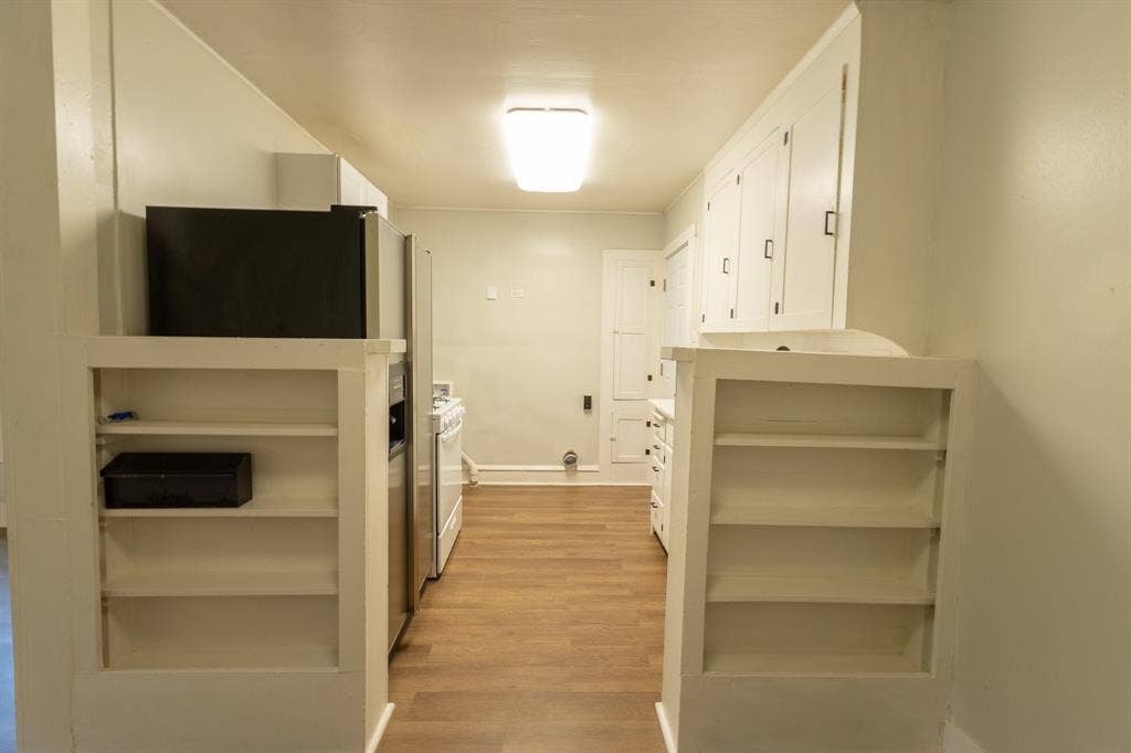 613 N 23rd Street, #15, Waco, TX 76707 Galley kitchen featuring wood-finish flooring, white built-in shelving, stainless steel refrigerator, white range, and white cabinetry