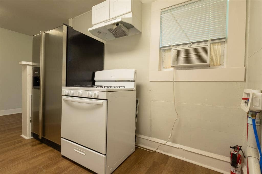 613 N 23rd Street, #15, Waco, TX 76707 Kitchen area featuring wood-finish flooring, a white gas range with overhead exhaust, stainless steel refrigerator with an ice/water dispenser, and a window with an integrated air conditioning unit