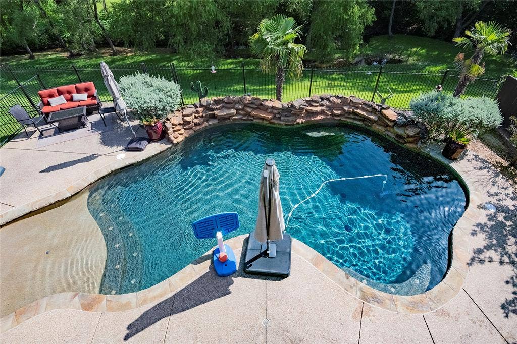 Freeform swimming pool featuring a rock waterfall, integrated steps, and surrounding concrete decking with Oklahoma flagstone coping