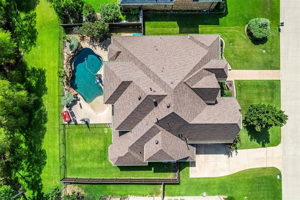 Expansive property featuring a multi-gabled roofline, lush green lawns, a freeform swimming pool with integrated rock features, perimeter fencing, and mature trees
