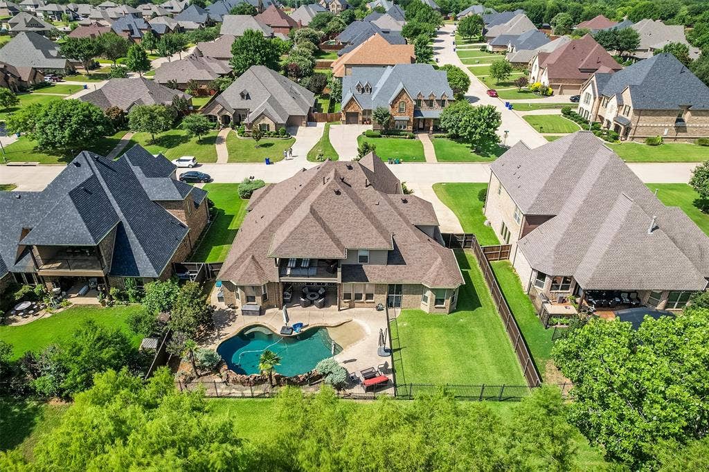Aerial perspective of a property featuring a curvilinear pool with integrated rock waterfall features, large backyard and lush green landscape in back