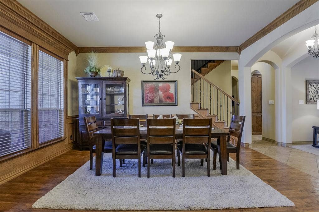 Open dining area featuring wood-finish flooring, an ornate chandelier, arched doorways, and a staircase with wrought iron balusters