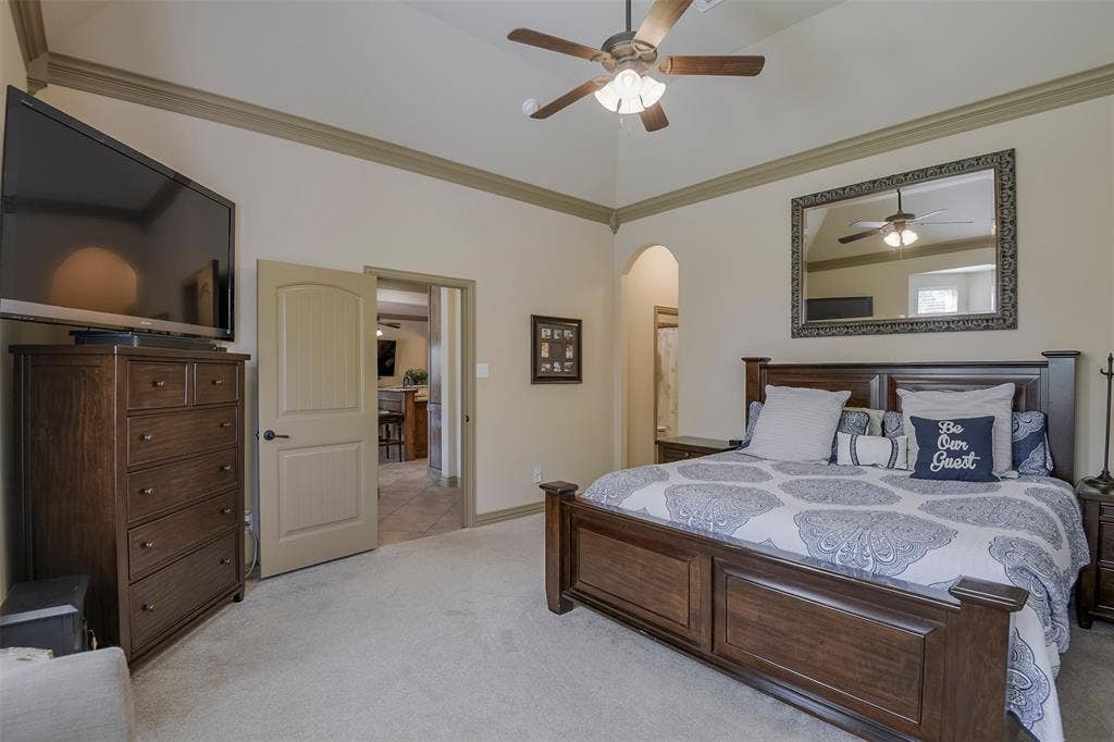Upstairs spacious sleeping quarters featuring vaulted ceilings, crown molding, a ceiling fan, and carpeted flooring