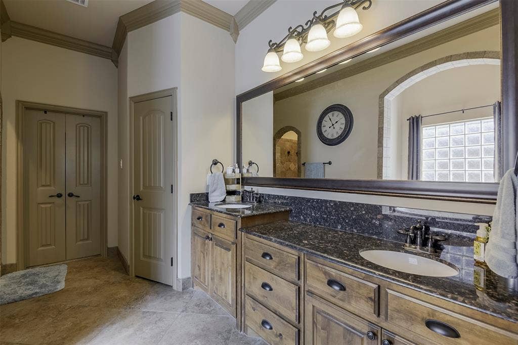 Bathroom featuring an expansive vanity with double sinks, dark stone countertops, wood cabinetry, and a large framed mirror