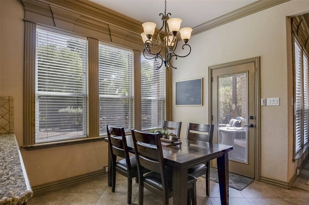 Dining area with a multi-pane glass door, three large windows, a decorative chandelier, tile flooring, and crown molding