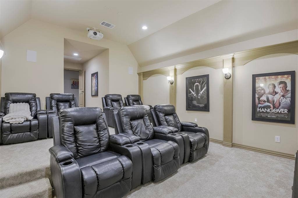 Dedicated media room featuring tiered seating, recessed lighting, wall sconces, ceiling-mounted projector, and integrated wall speakers