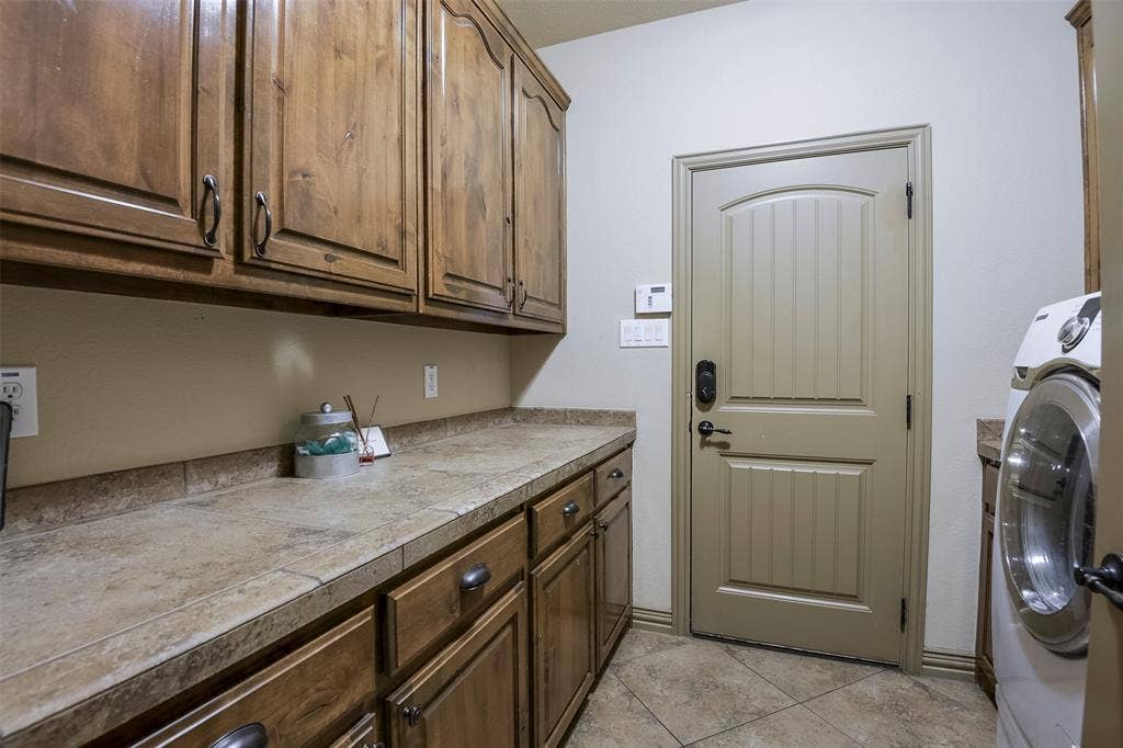 Utility room featuring extensive wood cabinetry, a durable countertop, tiled flooring, and a paneled door