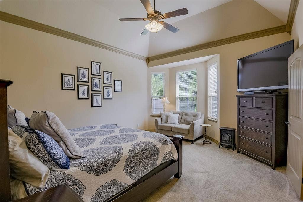 Additional downstairs ensuite bedroom, vaulted ceiling with crown molding, ceiling fan, and carpeted flooring.