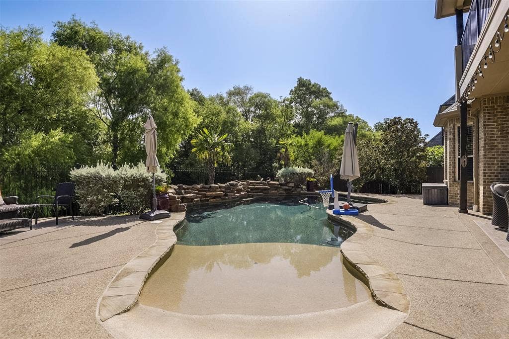 Freeform swimming pool with a stone waterfall feature, expansive concrete decking, and mature landscaping