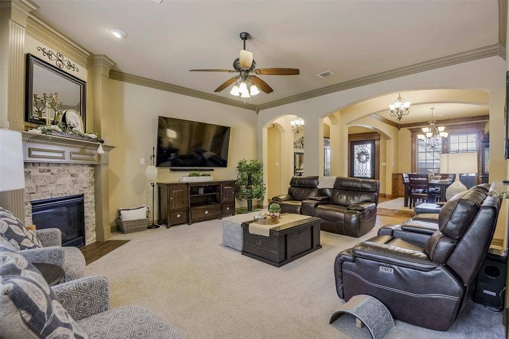 Living area featuring light-toned carpeting, a ceiling fan with integrated lighting, and crown molding