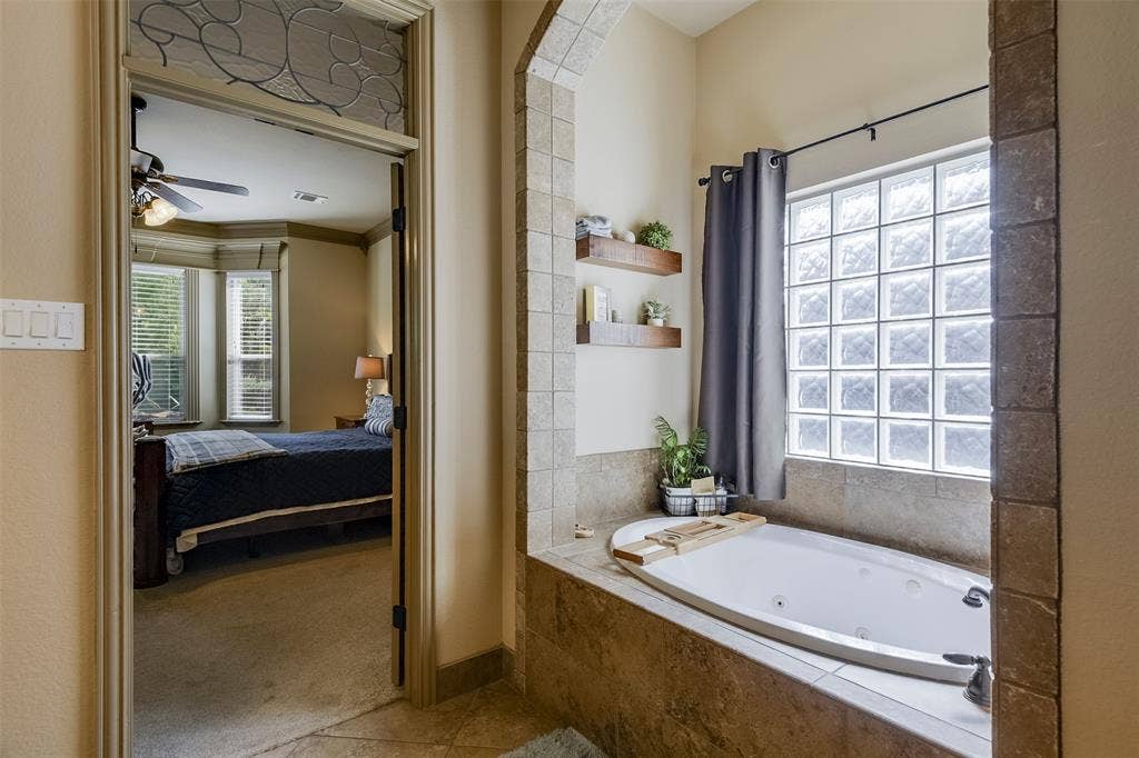 Spa-style jetted tub with stone tile surround and privacy glass block window
