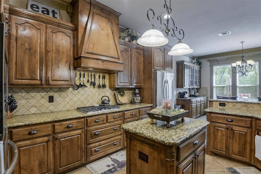 Spacious kitchen featuring custom wood cabinetry, granite countertops, a built-in gas range, and a central island with additional storage