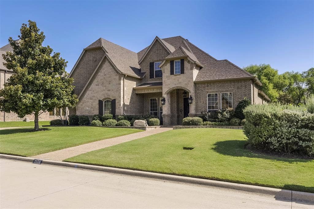 Stately brick and stone facade residence featuring a covered entry, dark shutters, and mature landscaping