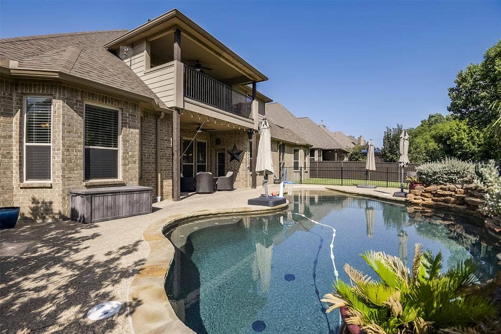 Custom-shaped swimming pool with a stone waterfall feature and surrounding aggregate concrete decking