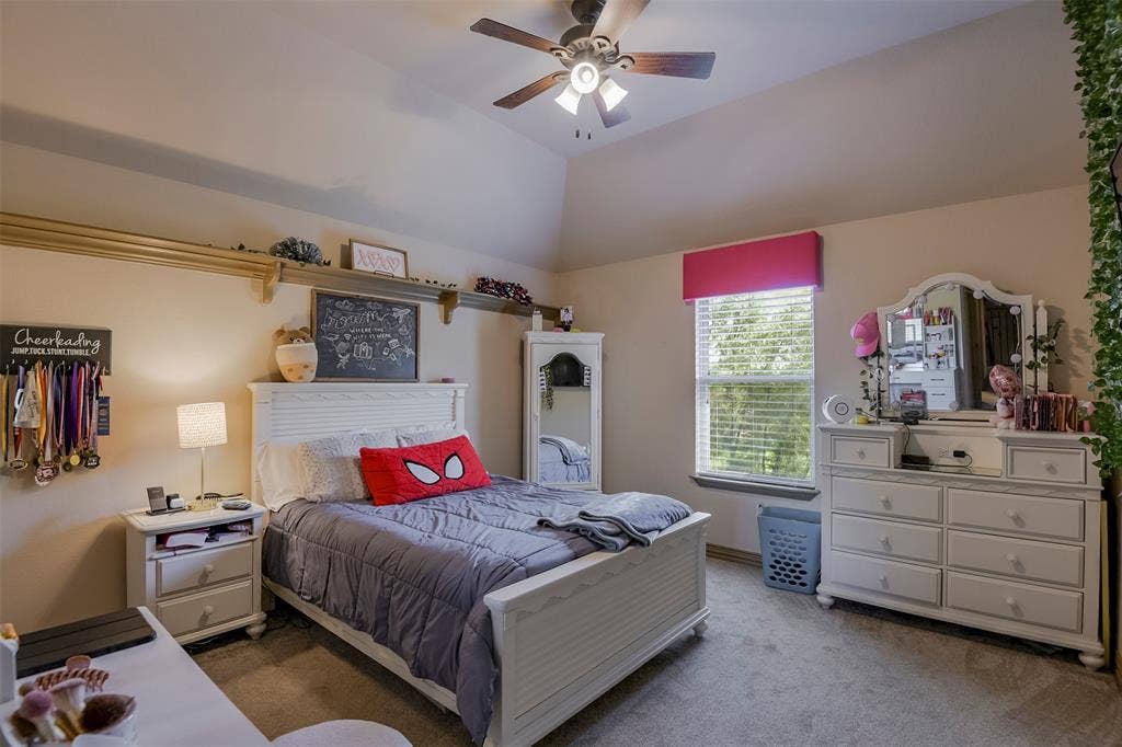 Carpeted bedroom featuring a vaulted ceiling with a ceiling fan, a window with blinds, and built-in shelving