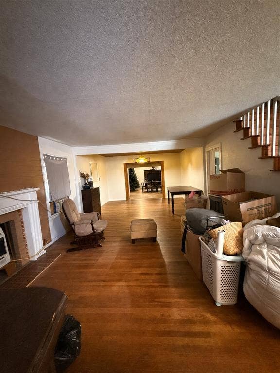311 S Ebrite Street, Mesquite, TX 75149 Spacious living area featuring wood-finish flooring, a traditional brick fireplace with a white mantel, and a staircase with open risers and wood handrails