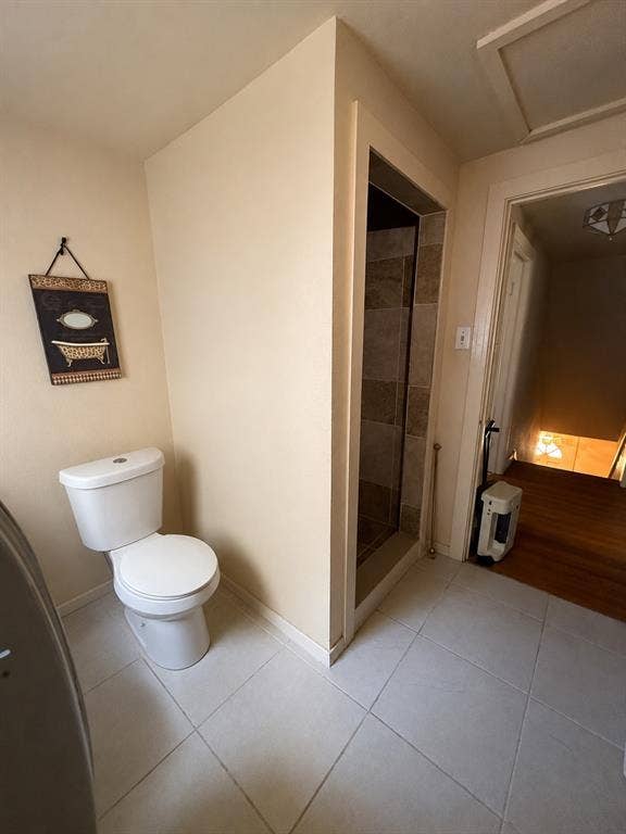 311 S Ebrite Street, Mesquite, TX 75149 Bathroom featuring a white toilet, tile flooring, and a walk-in shower with stone-look tile surround and glass enclosure