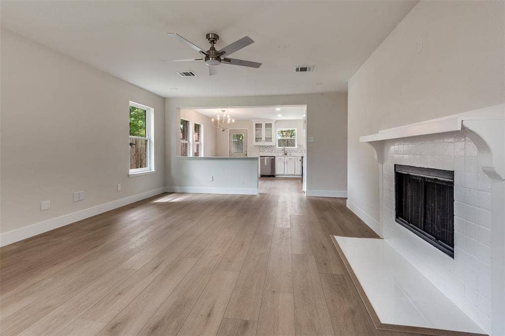 Living area featuring wood-finish flooring, a contemporary ceiling fan, and a tiled fireplace with a mantel