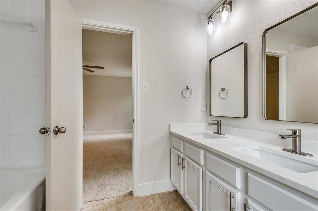 Bathroom featuring a dual vanity with white cabinetry, integrated sinks, and brushed nickel fixtures