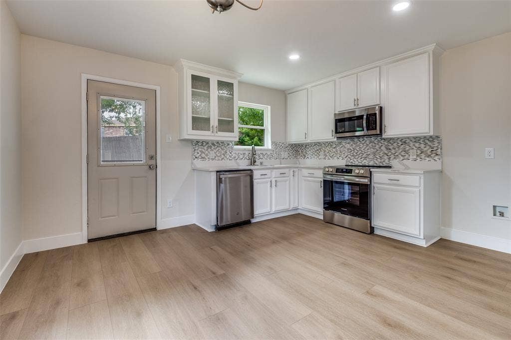 Modern kitchen featuring white cabinetry with brushed nickel hardware, stainless steel appliances, mosaic tile backsplash, and light wood-finish flooring