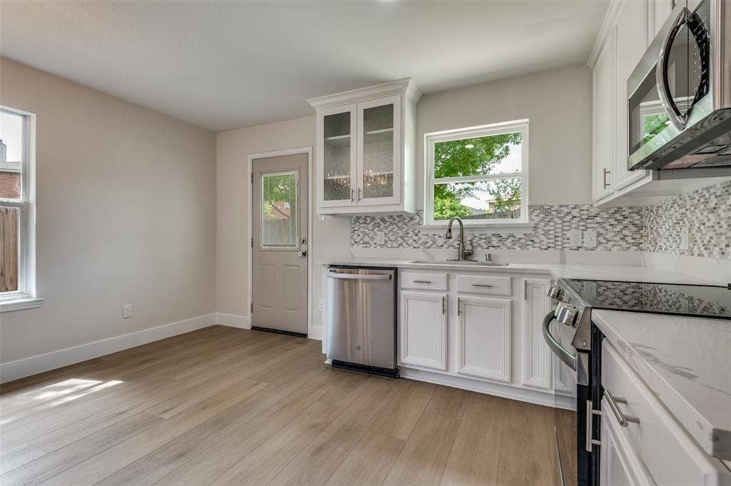 Modern kitchen featuring white cabinetry, stainless steel appliances, a mosaic tile backsplash, and quartz countertops