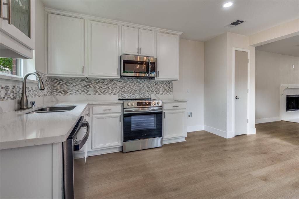 Kitchen featuring white cabinetry, stainless steel appliances, mosaic tile backsplash, white countertops, and wood-finish flooring