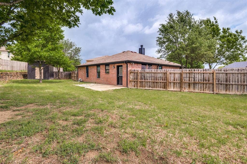 Spacious backyard featuring a brick exterior, privacy fencing, mature trees, and a concrete patio pad