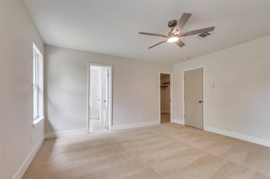 Neutral-toned carpeting spans this spacious room, featuring a modern ceiling fan with integrated lighting