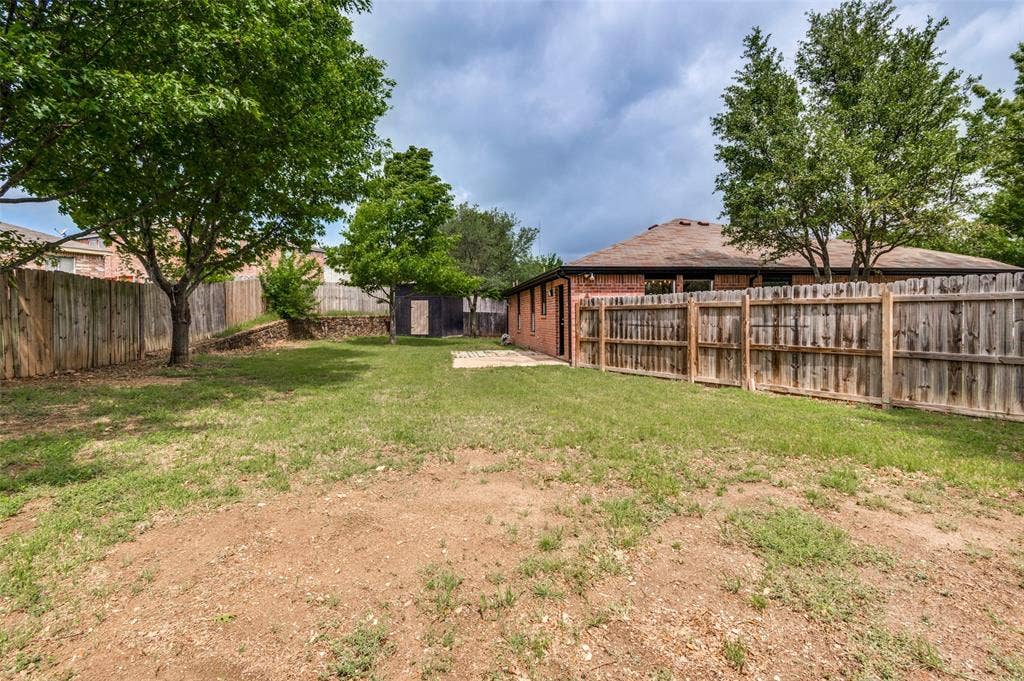 Spacious backyard featuring wood fencing, mature trees, and a storage shed